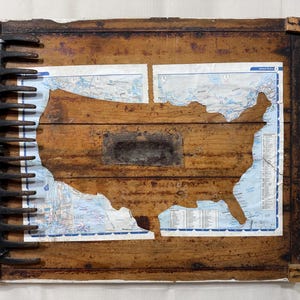 May include: A rectangular wooden board featuring a cutout of the United States map layered over a paper map. A dark metal rake head is attached to the left side, and a small rectangular metal mesh piece is centered over the wooden map cutout.