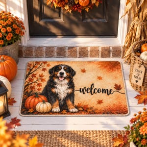 Peut inclure: Un paillasson rectangulaire illustré d'un bouvier bernois assis parmi des citrouilles orange et des feuilles d'automne tombées. Le mot welcome est imprimé en écriture noire sur la droite. Le fond représente une scène automnale dorée.