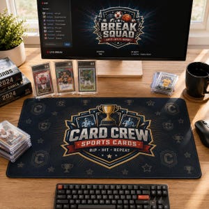 May include: A rectangular black desk mat featuring a central graphic with a gold trophy, two baseball players, and the text "CARD CREW SPORTS CARDS RIP HIT REPEAT" in white and red, surrounded by a pattern of small stars, trophies, and the letter C.