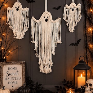 May include: Three off-white macrame ghost wall hangings with knotted cord details and black felt eyes. Each ghost features a rounded head and long, flowing fringe strands hanging downward, suspended by a simple cord loop for wall mounting.