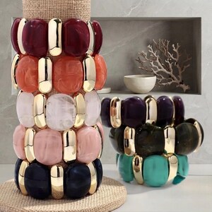 Peut inclure: Une collection de bracelets extensibles composés de barres métalliques dorées polies alternant avec des perles en résine marbrée arrondies, déclinées en rouge foncé, orange, blanc, rose clair, bleu marine, violet, vert foncé et turquoise.