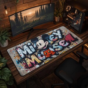 Puede incluir: Una alfombrilla de escritorio rectangular con una ilustración estilo grafiti de Mickey Mouse con pantalones cortos rojos. El diseño incluye letras grandes y estilizadas que forman la palabra "MICKEY" con una estética de salpicaduras.