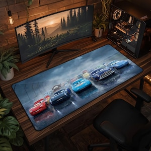Puede incluir: Una alfombrilla de escritorio rectangular con una impresión gráfica de alta resolución de varios coches de carreras antropomórficos de la película Cars, incluyendo un coche rojo, uno azul y uno azul oscuro, conduciendo sobre una pista de asfalto gris.