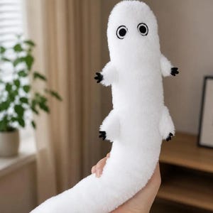 May include: A white plush toy shaped like a long, slender creature with a soft, fuzzy texture. It features two large, circular black and white eyes positioned near the top and four small limbs ending in black, claw-like tips on its elongated body.