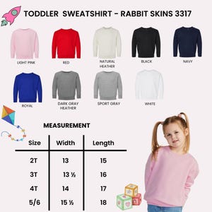 Op de afbeelding: Een collectie Rabbit Skins 3317 peutersweatshirts in lichtroze, rood, naturel heather, zwart, marineblauw, koningsblauw, donkergrijs heather, sportgrijs en wit. Een maattabel toont de breedtes en lengtes in inches voor de maten 2T tot 5/6.