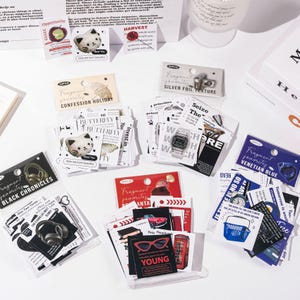 May include: A collection of multiple packs of decorative stickers featuring various themes, including black and white illustrations, vintage cars, red telephone booths, headphones, and text-based designs, all organized in clear plastic packaging.