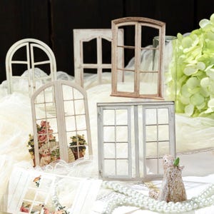 Könnte beinhalten: Eine Sammlung von Miniatur-Fensterrahmen in verschiedenen Formen und Ausführungen, darunter gewölbte und rechteckige Designs mit weißer und holzfarbener Lackierung. Einige Rahmen haben Gittermuster, andere zeigen kleine Blumen- und Tiermotive.