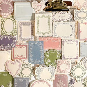 May include: A collection of assorted paper stickers and labels featuring intricate decorative frames, floral motifs, and bows in various shapes and muted colors. Some labels include text such as Regards, DIPLOMA, and AWESOME QUALITY.