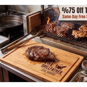 May include: A rectangular bamboo cutting board featuring a laser-engraved design that reads THE GRILLFATHER and LUCAS RODRIGUEZ with a flame icon. A cooked steak rests on the board, while a grill with meat and metal tongs are visible nearby.