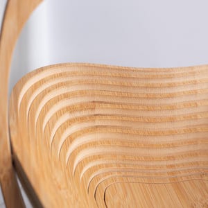 May include: A light brown wooden basket featuring a collapsible design with a series of concentric, wavy, layered slats that form a deep, open bowl shape. The structure is crafted from thin, flexible wood panels with a natural grain finish.