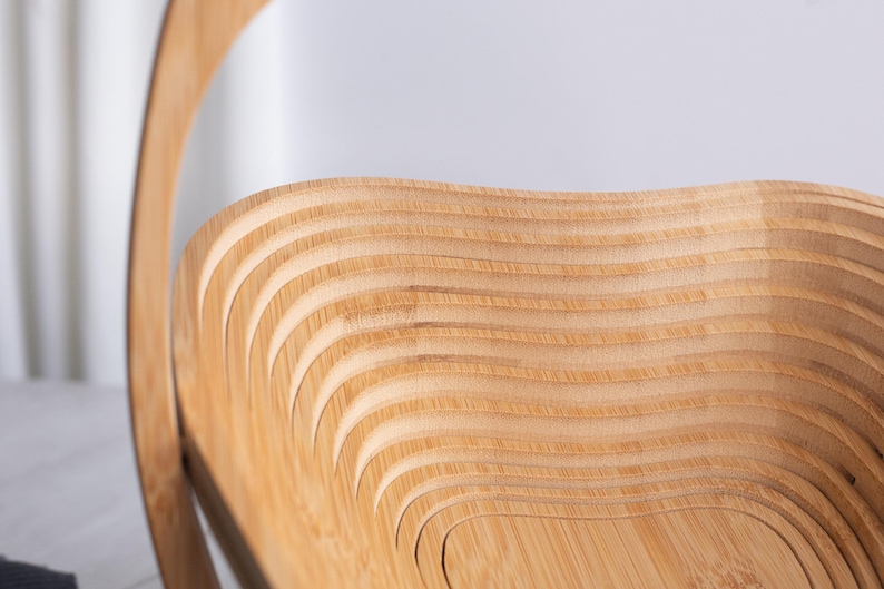 May include: A light brown wooden basket featuring a collapsible design with a series of concentric, wavy, layered slats that form a deep, open bowl shape. The structure is crafted from thin, flexible wood panels with a natural grain finish.