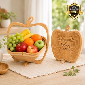May include: A collapsible bamboo fruit basket shaped like an apple, filled with green grapes, bananas, an orange, and two apples. Beside it stands a matching folded bamboo apple-shaped board engraved with the text The Williams Family.