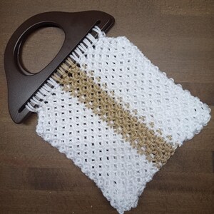 Puede incluir: Un bolso peque&ntilde;o con cuerpo de cord&oacute;n de macram&eacute; blanco y tostado con un patr&oacute;n de celos&iacute;a en forma de diamante. El bolso est&aacute; unido a un asa r&iacute;gida de pl&aacute;stico de color marr&oacute;n oscuro en forma de semic&iacute;rculo con un centro recortado.