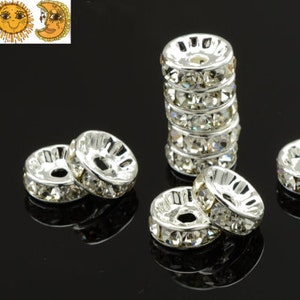 May include: A group of silver and clear crystal spacer beads. The beads are round and have a hole in the center. The beads are arranged in a circle on a black surface.