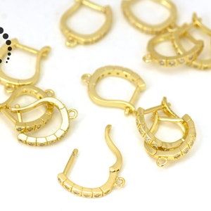 May include: A group of gold-toned earring findings with clear cubic zirconia stones. The findings are in the shape of a hoop with a small loop at the top for attaching a dangle.