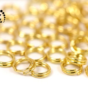 Puede incluir: Primer plano de anillas doradas, ideales para la fabricación de joyas o manualidades. Las anillas son de doble bucle y tienen un acabado brillante. Un logotipo con una "Z" estilizada está en la esquina superior izquierda.