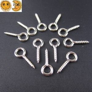 Puede incluir: Primer plano de doce ojetes de tornillo plateados con un bucle redondo. Los ojetes est&aacute;n dispuestos en un c&iacute;rculo sobre una superficie gris oscuro.