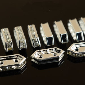 May include: A set of ten silver-toned metal embellishments with clear rhinestones. The embellishments are in two different shapes: rectangular and hexagonal.