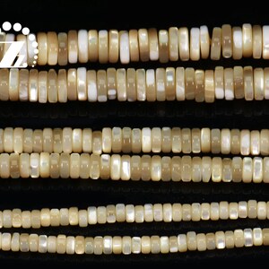 May include: Close-up of multiple strands of rectangular, iridescent beads in cream and tan hues. The beads are uniform in size and shape, creating a textured surface. These beads are likely for jewellery making.