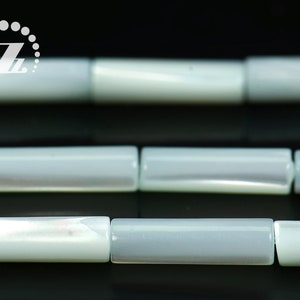 Peut inclure: Un brin de perles de coquillage gris clair et blanc, chaque perle est de forme cylindrique rectangulaire.