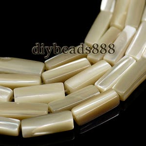 Peut inclure: Un brin de perles rectangulaires en coquillage beige et blanc. Les perles ont une surface lisse et polie et un léger éclat iridescent.