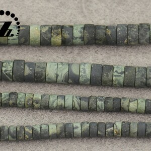 May include: Strands of flat, cylindrical beads in shades of green and gray. The beads have a mottled, marbled appearance, suggesting a natural stone material. The beads are strung together, ready for jewelry making or other crafts.