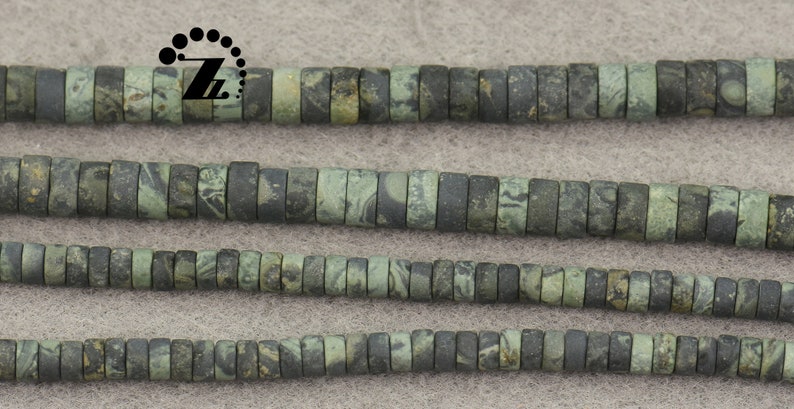May include: Strands of flat, cylindrical beads in shades of green and gray. The beads have a mottled, marbled appearance, suggesting a natural stone material. The beads are strung together, ready for jewelry making or other crafts.