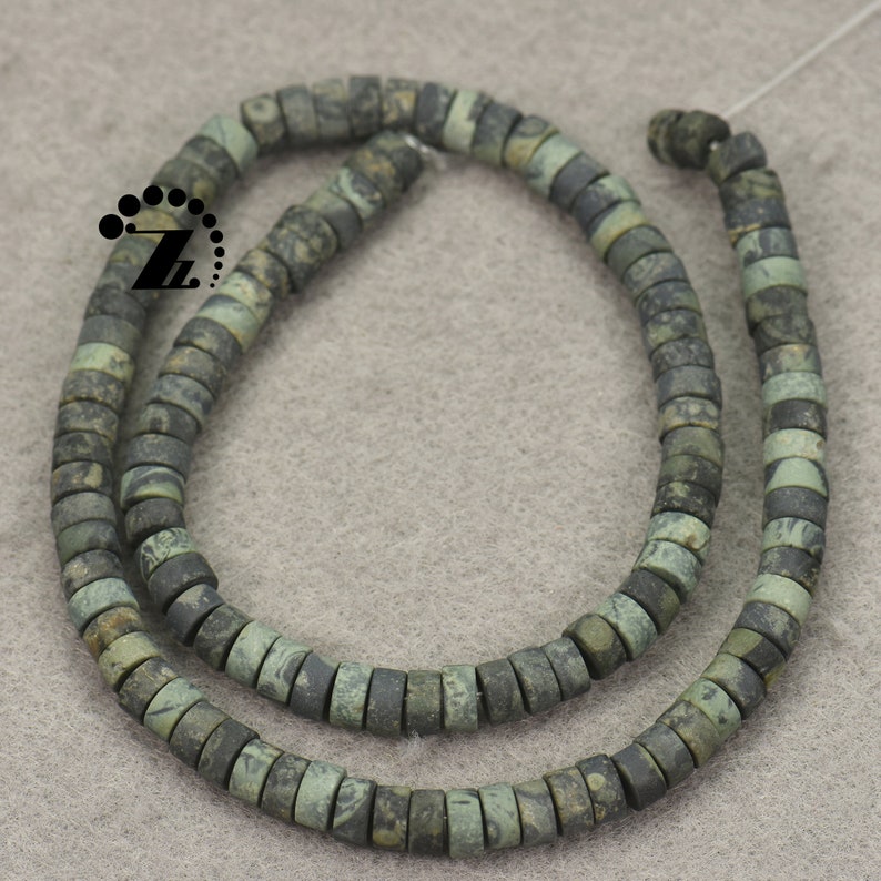 May include: Strands of flat, round beads in shades of green and gray. The beads have a mottled appearance, suggesting a natural stone material. The beads are strung together, forming a necklace or bracelet.