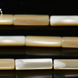 以下が含まれることがあります： ベージュと白の貝殻ビーズのストランド。ビーズは長方形で、滑らかで磨かれた仕上げになっています。