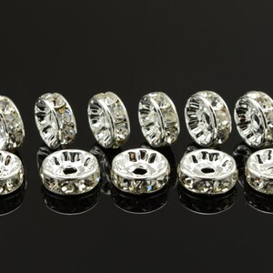 May include: Ten silver-toned bead caps with clear rhinestone accents. The bead caps are round and have a hole in the center.
