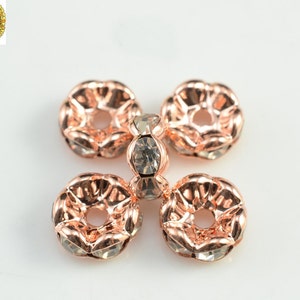 May include: Five rose gold-toned metal bead caps with clear rhinestone accents. The bead caps are round with a hole in the center.