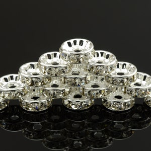 May include: A group of silver-toned metal bead caps with clear rhinestones around the edge. The bead caps are stacked in a pyramid shape.