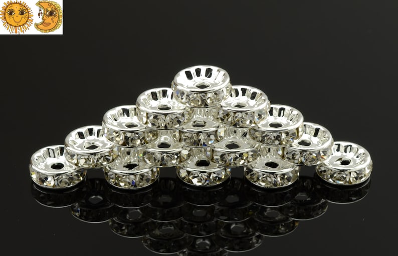 May include: A group of silver-toned metal bead caps with clear rhinestones around the edge. The bead caps are stacked in a pyramid shape.