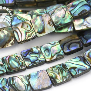 May include: A strand of square-shaped iridescent abalone shell beads. The beads have a dark brown border and a swirling pattern of blue, green, and gold.