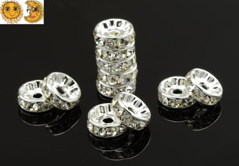 May include: A group of silver and clear crystal spacer beads. The beads are round and have a hole in the center. The beads are arranged in a circle on a black surface.