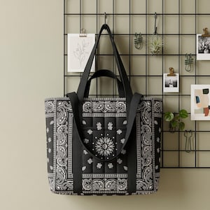 Può includere: Una borsa tote trapuntata nera con un motivo bandana paisley bianco. La borsa presenta due paia di manici in tessuto nero, inclusi manici corti e tracolle più lunghe, con una forma rettangolare strutturata e dettagli impunturati.
