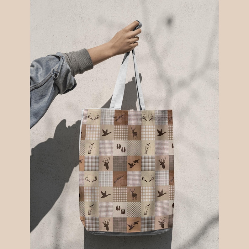 May include: A tote bag featuring a patchwork pattern of beige, brown, and white squares. The design includes repeating icons of deer antlers, silhouettes of deer, ducks in flight, hunting rifles, animal tracks, and tall grass stalks.