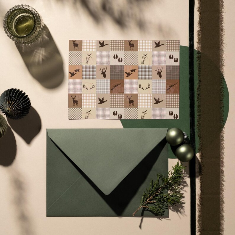 May include: A rectangular card featuring a grid pattern of brown and beige squares with silhouettes of deer, ducks, antlers, tracks, and reeds, paired with a dark olive green envelope and a small sprig of evergreen needles.