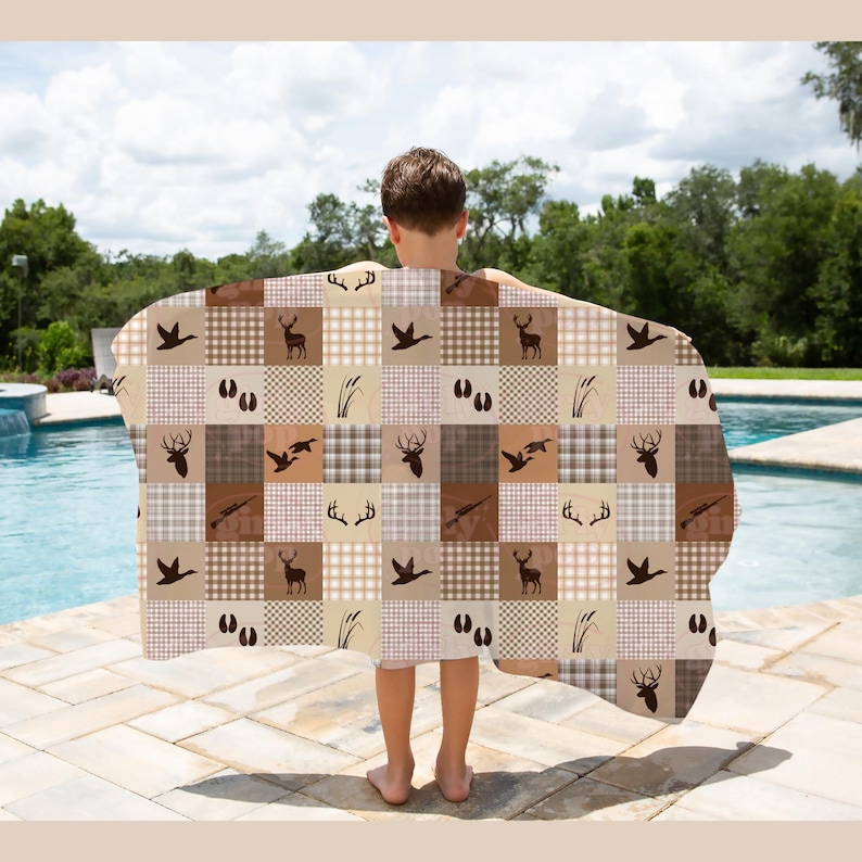 May include: A rectangular blanket featuring a patchwork pattern of brown and beige squares. The design includes repeating silhouettes of deer, antlers, ducks, animal tracks, and reeds, interspersed with solid colours and checkered patterns.