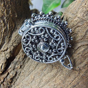 May include: A round silver-toned metal ring featuring an intricate embossed pattern with small raised dots and swirling lines. The circular face of the ring has a textured, oxidized finish with a central stud and a decorative scalloped border edge.