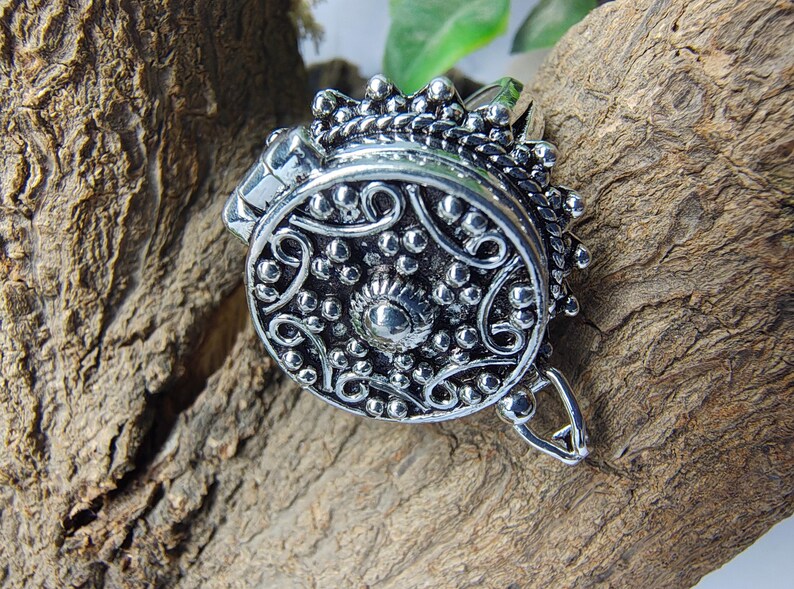 May include: A round silver-toned metal ring featuring an intricate embossed pattern with small raised dots and swirling lines. The circular face of the ring has a textured, oxidized finish with a central stud and a decorative scalloped border edge.