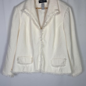 May include: An off-white textured tweed blazer featuring a notched collar, long sleeves, and two front pockets with frayed edges. The garment includes a front opening with frayed trim along the lapels and hem, and a label reading Sag Harbor.