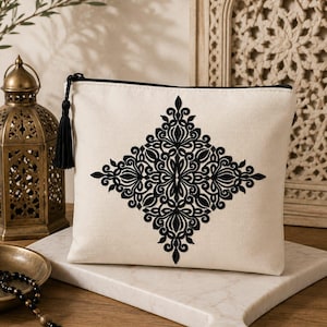 Peut inclure: Une pochette rectangulaire couleur crème dotée d'une fermeture éclair noire et d'un motif damassé noir brodé de manière symétrique au centre. La pochette est munie d'un pompon noir assorti attaché à la tirette de la fermeture éclair.