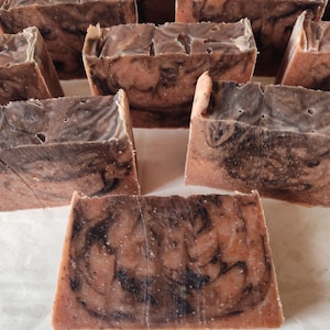 May include: A collection of handmade soap bars with a marbled design. The soap features a blend of brown and tan hues with dark swirls throughout. The bars are rectangular and appear to be freshly cut, showcasing a natural, artisanal aesthetic.
