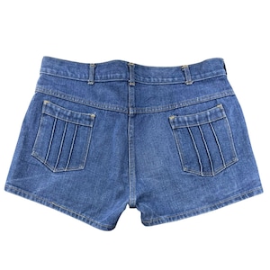 May include: A pair of medium-wash blue denim shorts featuring a high-waisted design with belt loops and two back pockets. Each back pocket is detailed with four vertical stitched pleats, and the garment is finished with gold-tone contrast stitching.