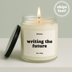 Peut inclure: Une bougie en pot de verre transparent avec une mèche allumée et un couvercle en métal noir posé sur le côté. L'étiquette blanche porte le texte 8Twelve, writing the future, et 8oz | 226g. La cire est blanc cassé dans un récipient cylindrique.