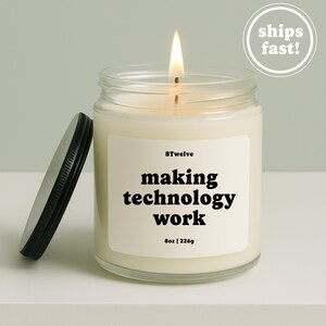Peut inclure: Une bougie en pot de verre transparent avec une mèche allumée et un couvercle en métal noir posé à côté. L'étiquette blanche porte le texte 8Twelve, making technology work, et 8oz | 226g. La cire est blanc cassé et la flamme est jaune et orange.
