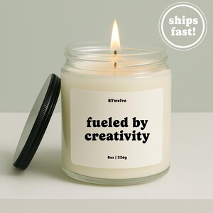 Peut inclure: Une bougie allumée dans un pot en verre transparent avec un couvercle en métal noir. L'étiquette blanche porte le texte 8Twelve, fueled by creativity, et 8oz | 226g. La cire est blanc cassé et la flamme est visible au sommet de la mèche.