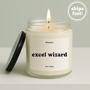 May include: A lit candle in a clear glass jar with a black lid. The white label features the text 8Twelve, excel wizard, and 8oz | 226g. The candle wax is off-white, and the flame is visible at the top of the wick, centered within the glass container.
