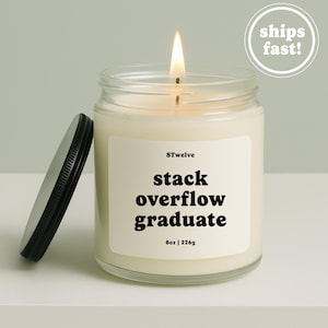 May include: A clear glass jar candle with a lit wick and a black metal lid placed to the side. The white label features the text 8Twelve, stack overflow graduate, and 8oz | 226g in black font. The wax is off-white and fills the cylindrical glass container.